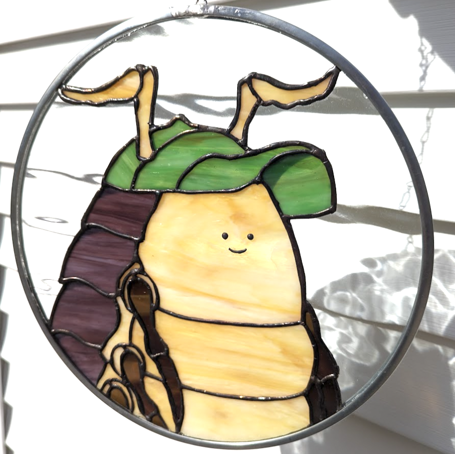 Image of a pillbug stained glass. It is about a foot across. The pillbug has a tiny smile and is wearing a green hat.